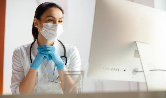 Masked healthcare professional watching computer