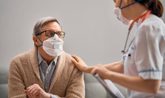 Masked patient and masked nurse in conversation